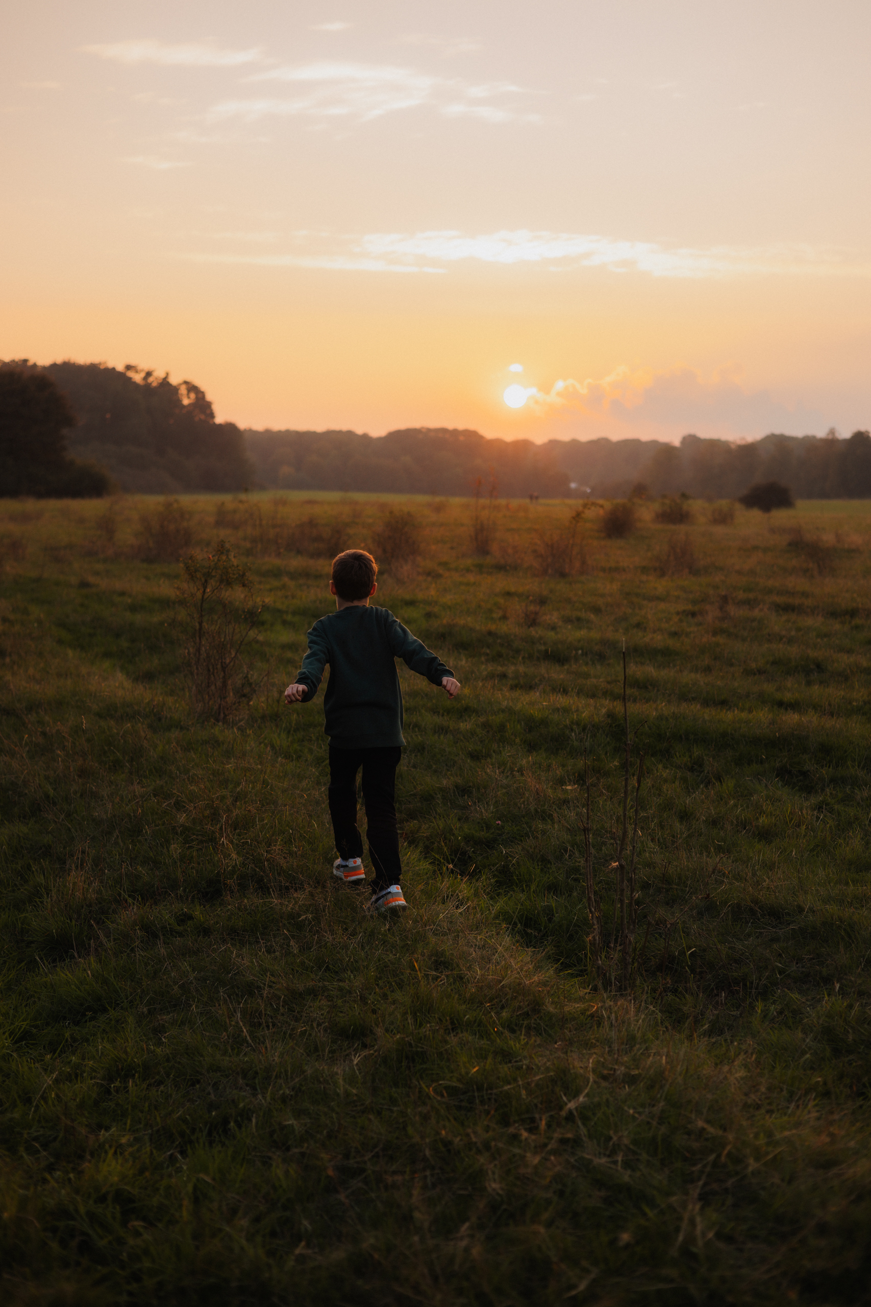 Junge läuft über eine große Wiese Richtung Sonnenuntergang