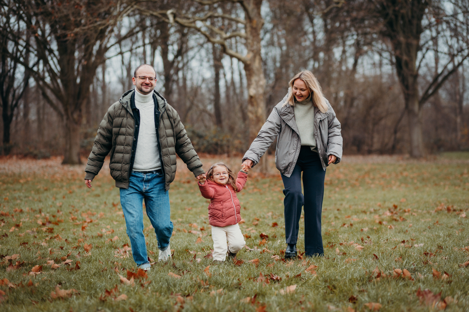 Eltern laufen mit Tochter an der Hand über Wiese – Familienfotografie Köln