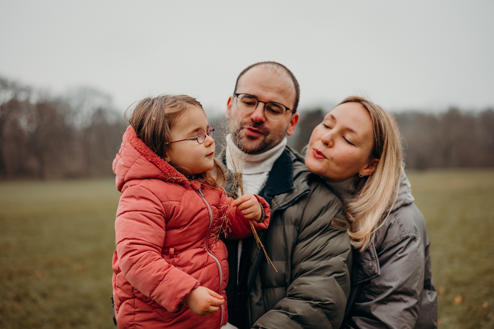 Eltern und kleine Tochter pusten gemeinsam eine Pusteblume in der Natur