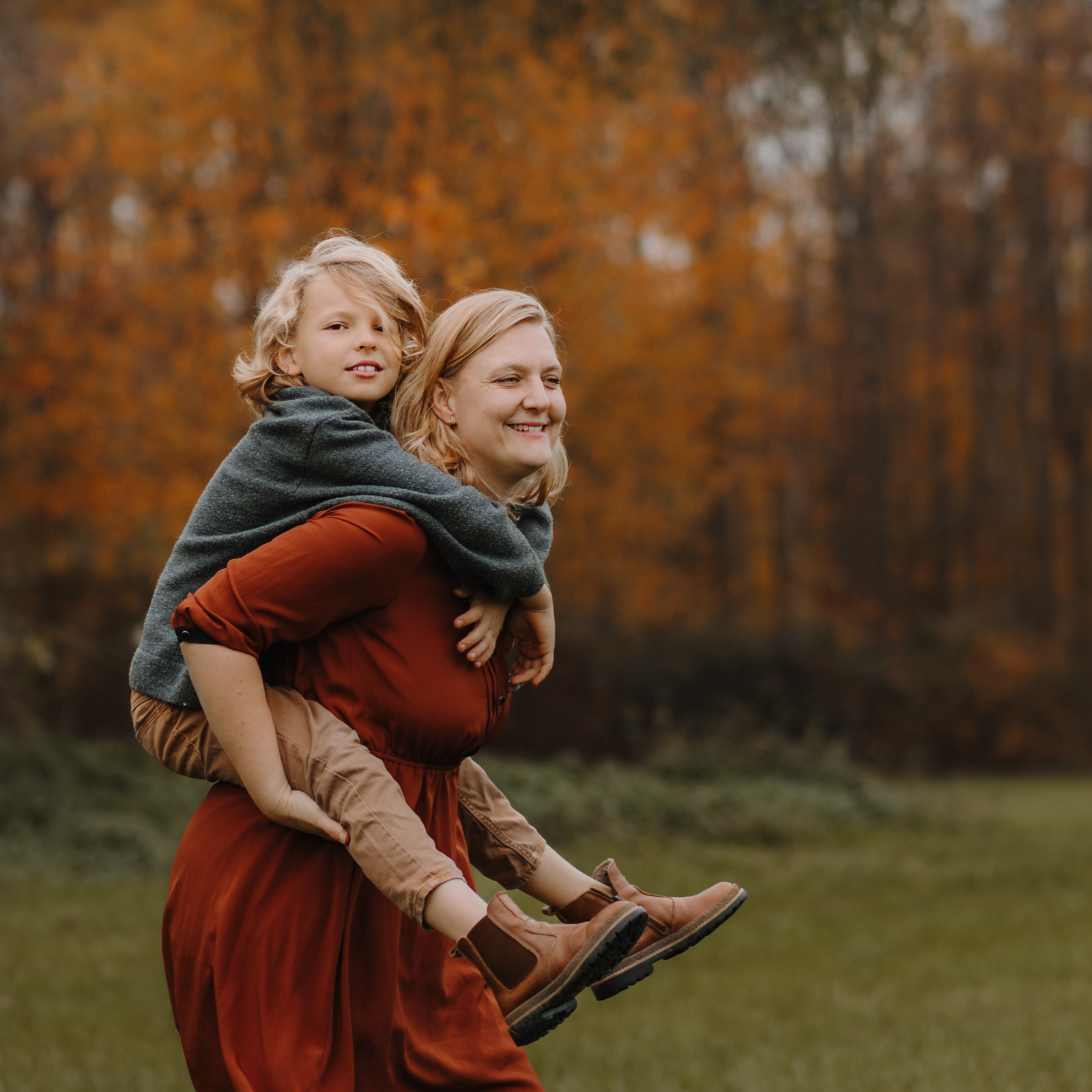 Sohn sitzt lächelnd huckepack auf seiner Mama beim Outdoor Fotoshooting in Köln