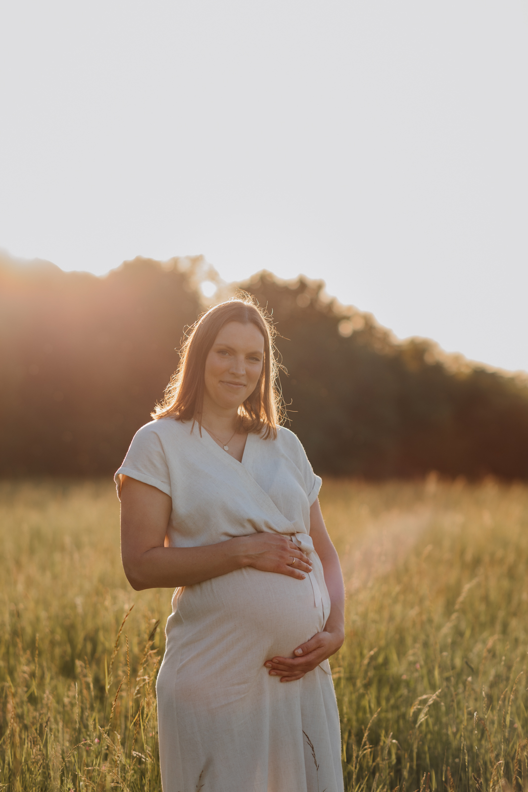 Werdende Mama lächelt zufrieden und voller Vorfreude in die Kamera bei Sonnenuntergang in der Natur