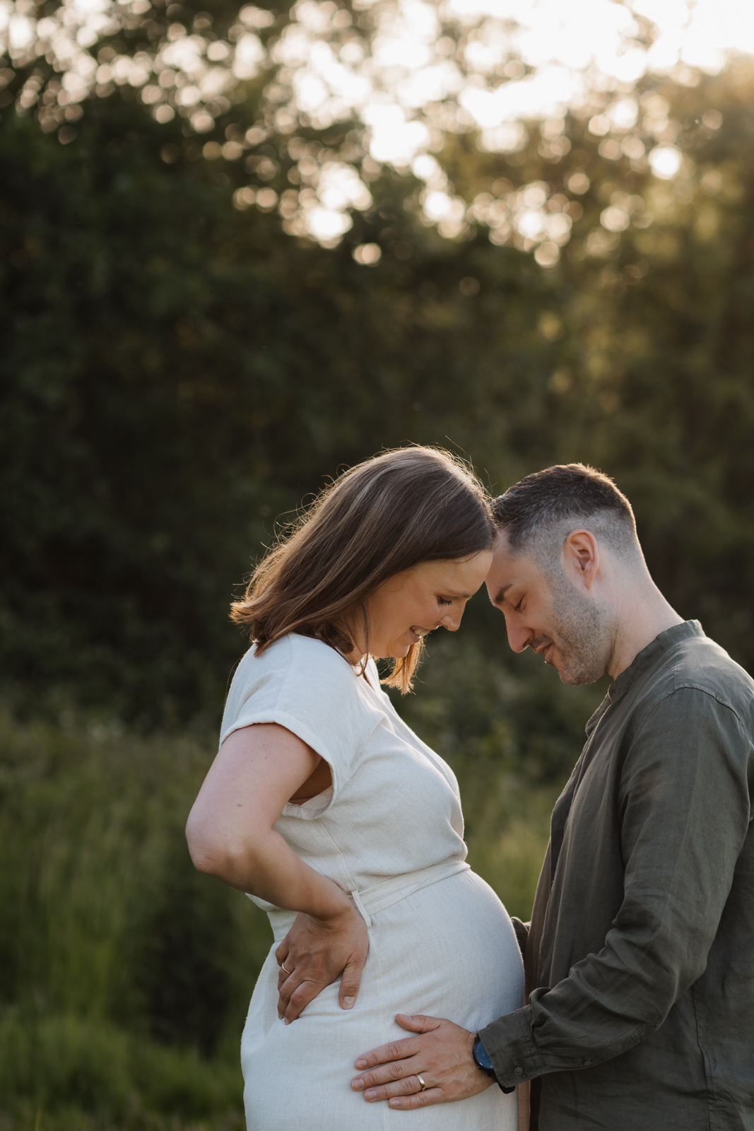 Werdende Eltern schauen voller Vorfreude gemeinsam auf den Babybauch, während der Papa schützend seine Hände darauf legt